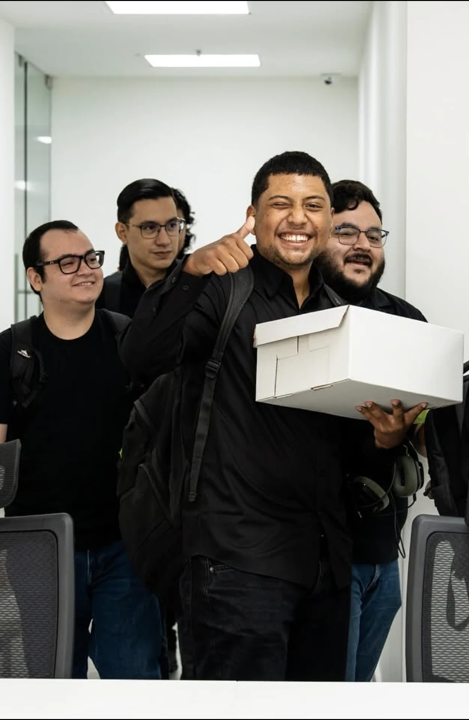 Colleagues laughing as one carries a box into the office, thumbs up.