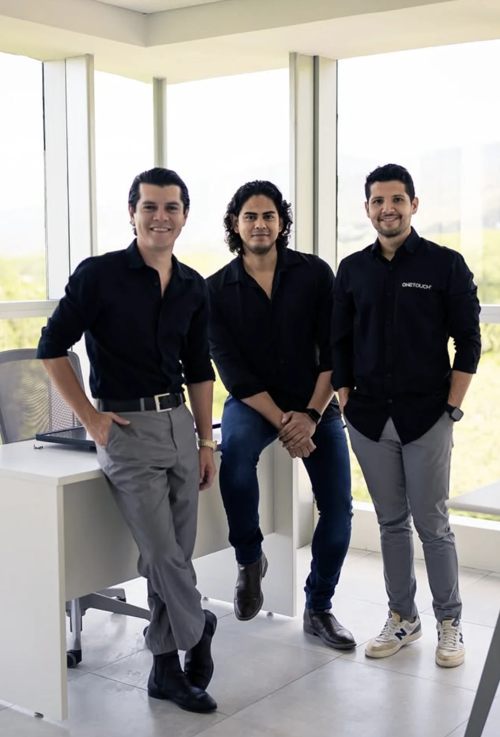 Three of the team by the floor-to-ceiling office windows.